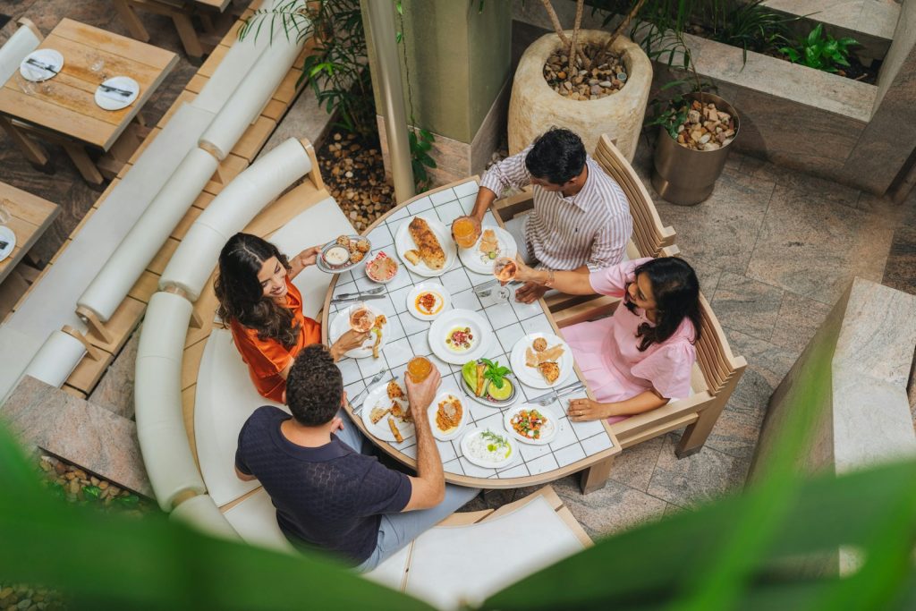 Cuatro personas comparten platos y bebidas en una mesa de azulejos al aire libre