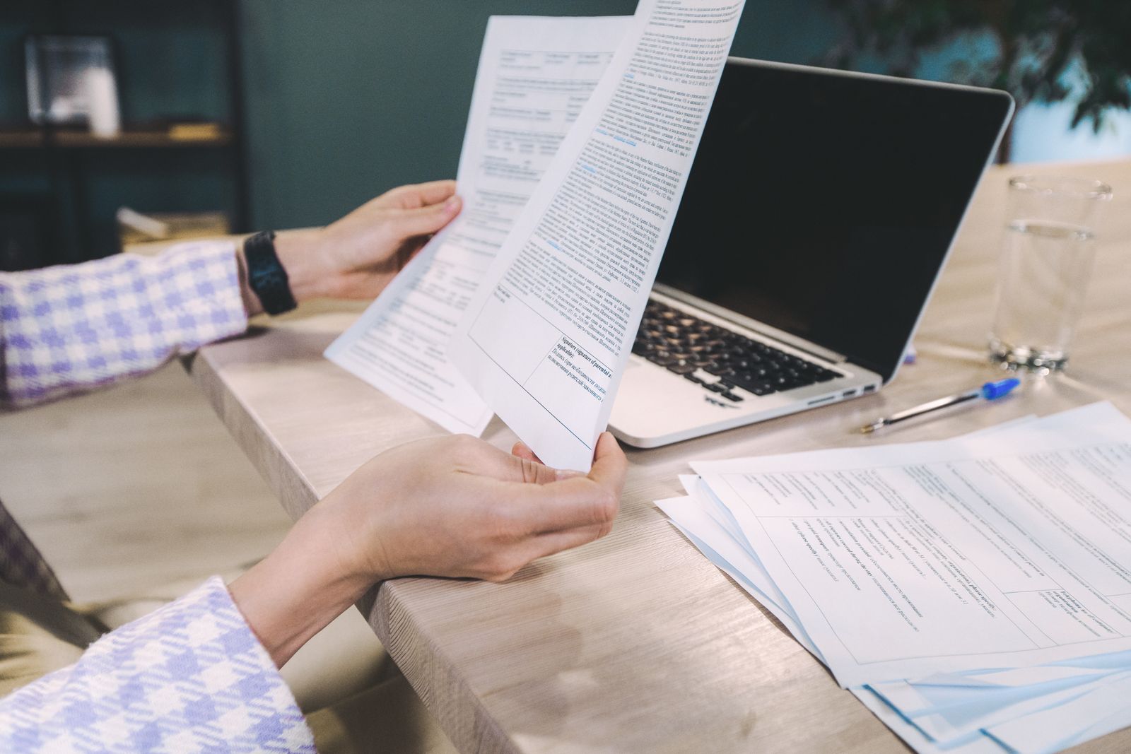 Manos examinando documentos impresos junto a un portátil sobre un escritorio de oficina