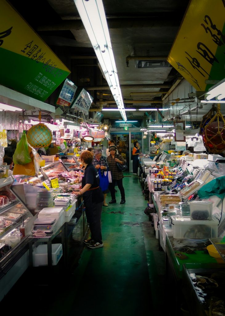 Personas haciendo la compra entre los puestos de un mercado cubierto con iluminación azulada