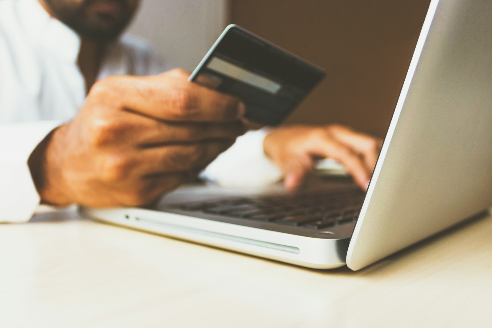 Persona sujetando una tarjeta bancaria mientras usa un ordenador portátil