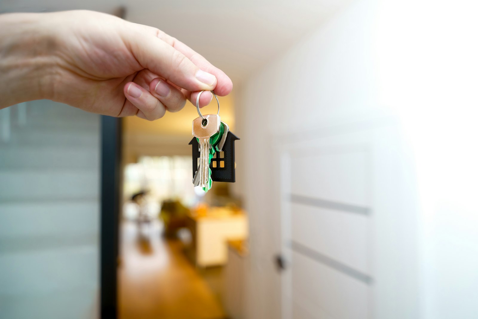 Mano que sostiene una llave de casa delante de la puerta de entrada de una vivienda